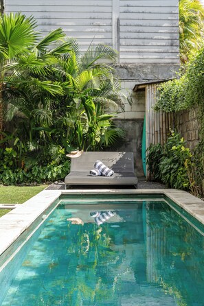 A swimming pool with a lounge chair and a surfboard, surrounded by lush greenery. - Villa Jungalow 2BR Pool Villa Near Beach Café del Mar & Padel (Canggu)