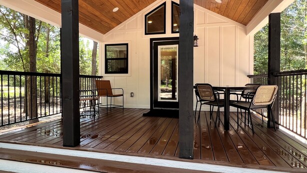 Un espacio al aire libre cubierto con una terraza de madera, una mesa con sillas y vistas a los árboles circundantes.