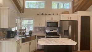 Una cocina con armarios blancos, una isla con encimera de mármol, electrodomésticos de acero inoxidable y techo de madera.