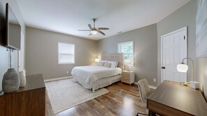 A bedroom with a bed, bedside tables, a desk, a chair, a ceiling fan, and a TV mounted on the wall.
