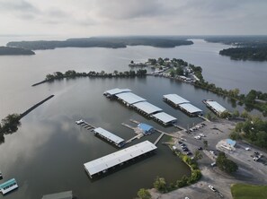 Une vue aérienne d’une marina où sont amarrés de nombreux bateaux, avec un espace de stationnement et un petit bâtiment doté d’un toit bleu.