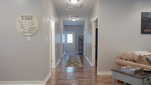 A hallway with hardwood floors, a rug, a couch, and a wall-mounted sign indicating Kentucky Lake coordinates. - Spacious Home in Moors Community on KY Lake with Outdoor Hot Tub and Fire Pit (Gilbertsville)