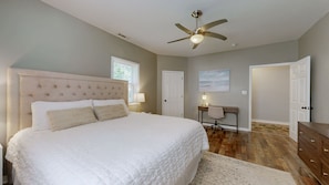 Une chambre avec un grand lit, un ventilateur de plafond, un bureau avec une chaise et une porte.