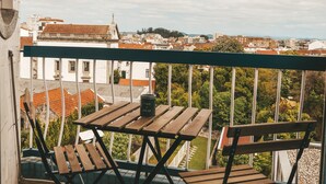 Un balcon avec une table et des chaises, donnant sur un paysage urbain avec des immeubles et des arbres.