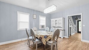 A dining room with a round table, six chairs, and a chandelier. There is a staircase leading to another level.