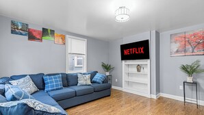 A modern living room with a sectional sofa, a flat-screen TV, and a bookshelf.