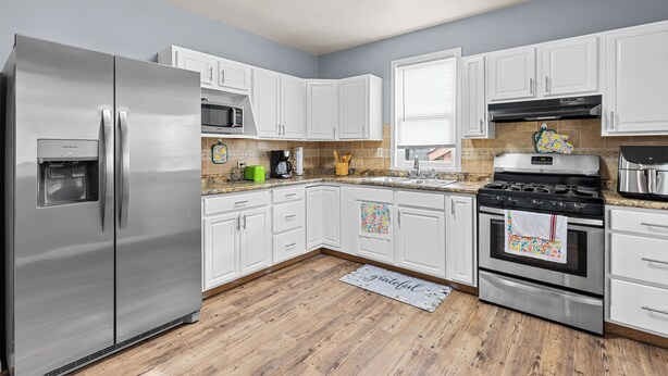 A modern kitchen with white cabinets, stainless steel appliances, and a wooden floor.