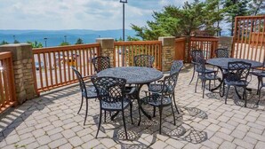 Une terrasse extérieure avec des tables et des chaises rondes, des piliers en pierre et une vue sur les montagnes.