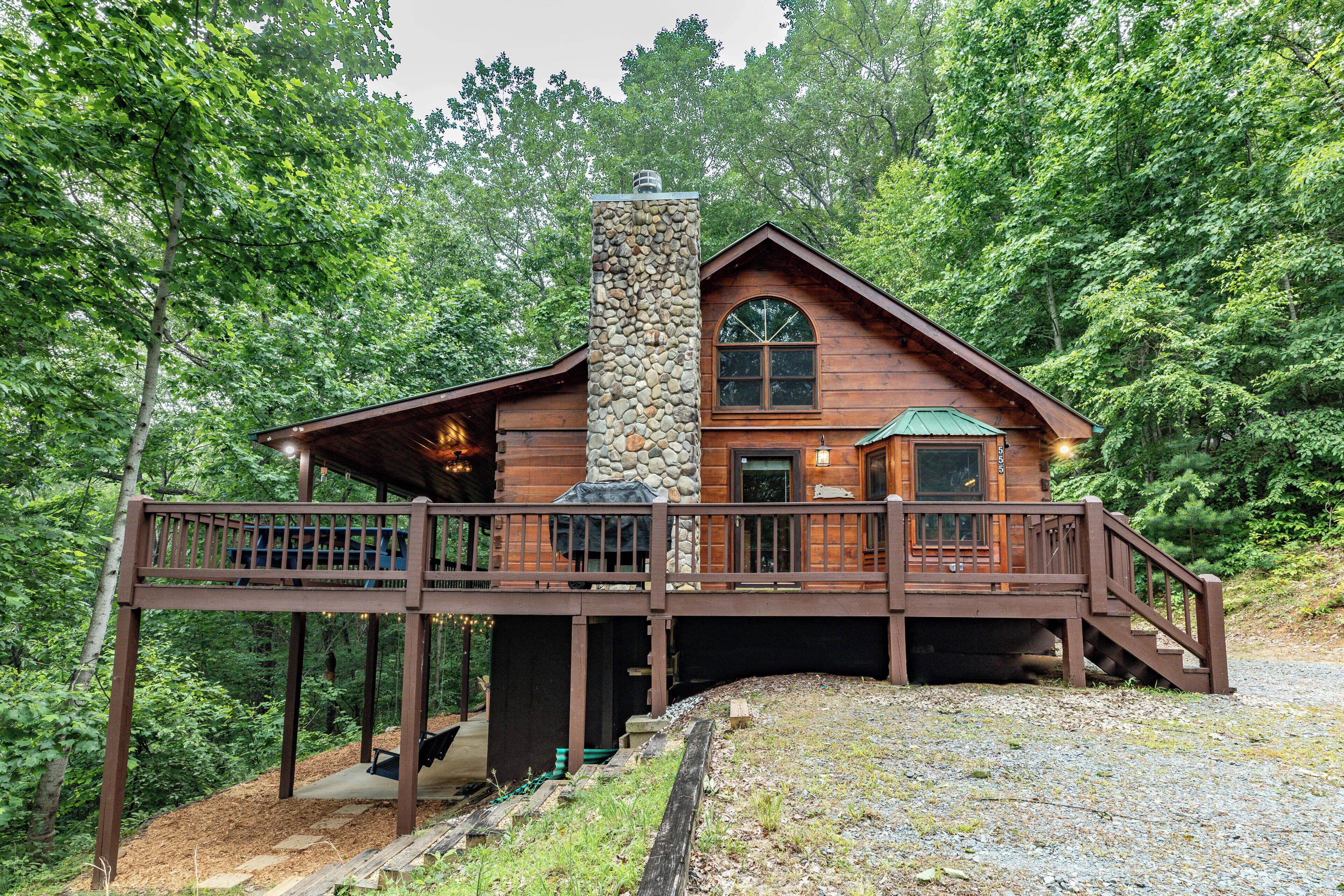 Une cabane en bois avec une cheminée en pierre, une terrasse et une vue sur la forêt environnante.