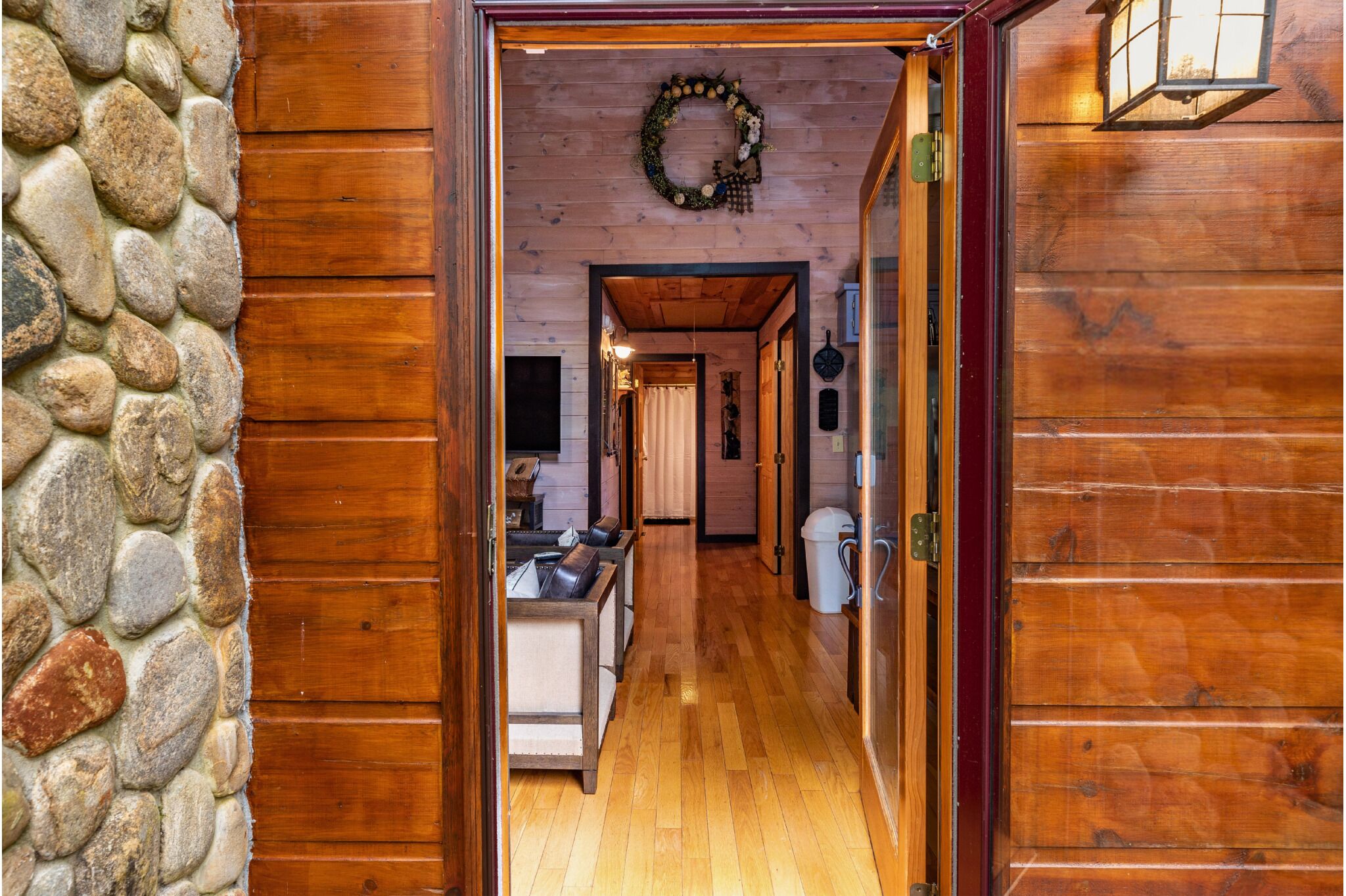 Un couloir intérieur en bois, avec un mur en pierre, une porte en bois et, au fond, on aperçoit un espace cuisine.