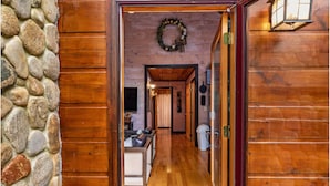 A wooden interior hallway with a stone wall, a wooden door, and a kitchen area visible in the background.