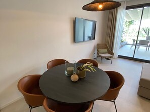 Un coin repas comprenant une table ronde, quatre chaises, un vase avec une plante et un téléviseur fixé au mur.