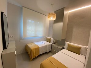 A hotel room with two beds, a bedside table, a mirror, and a window with blinds.