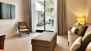 A modern living room with a sofa, a chair, a TV, and a sliding glass door leading to an outdoor area with a table and chairs.