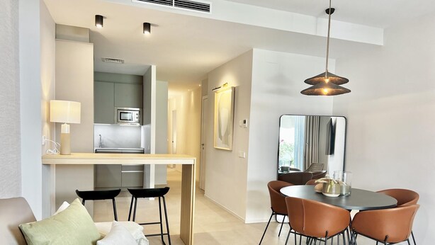 A modern living room with a sofa, a dining area with a table and chairs, and a kitchen in the background.