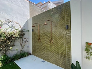 A modern outdoor shower area with a herringbone tile wall and copper fixtures.