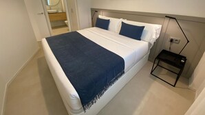 A modern bedroom with a large bed, a bedside table, and a wall-mounted lamp.