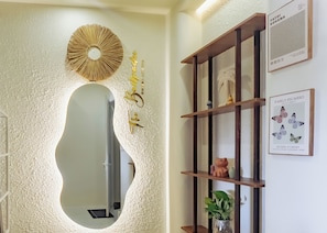 Un espace d’accueil agrémenté d’un grand miroir, d’une étagère en bois ornée d’objets décoratifs et d’œuvres d’art encadrées accrochées au mur.
