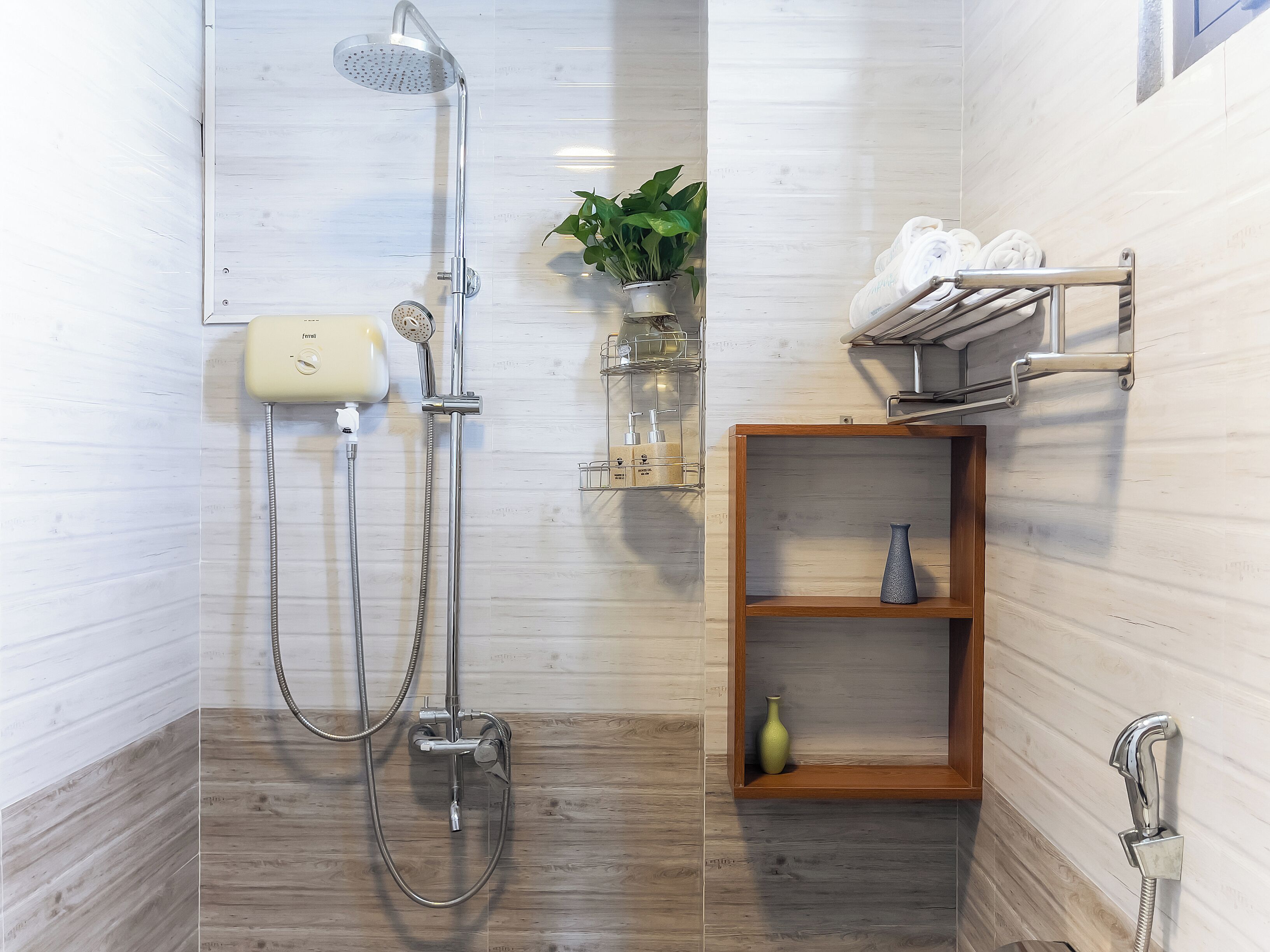 A modern bathroom with a shower, a towel rack, a shelf with a vase, and a potted plant.