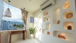 Una habitación moderna con un ventanal grande, un banco de madera, una planta en maceta y estantes en la pared con objetos decorativos.