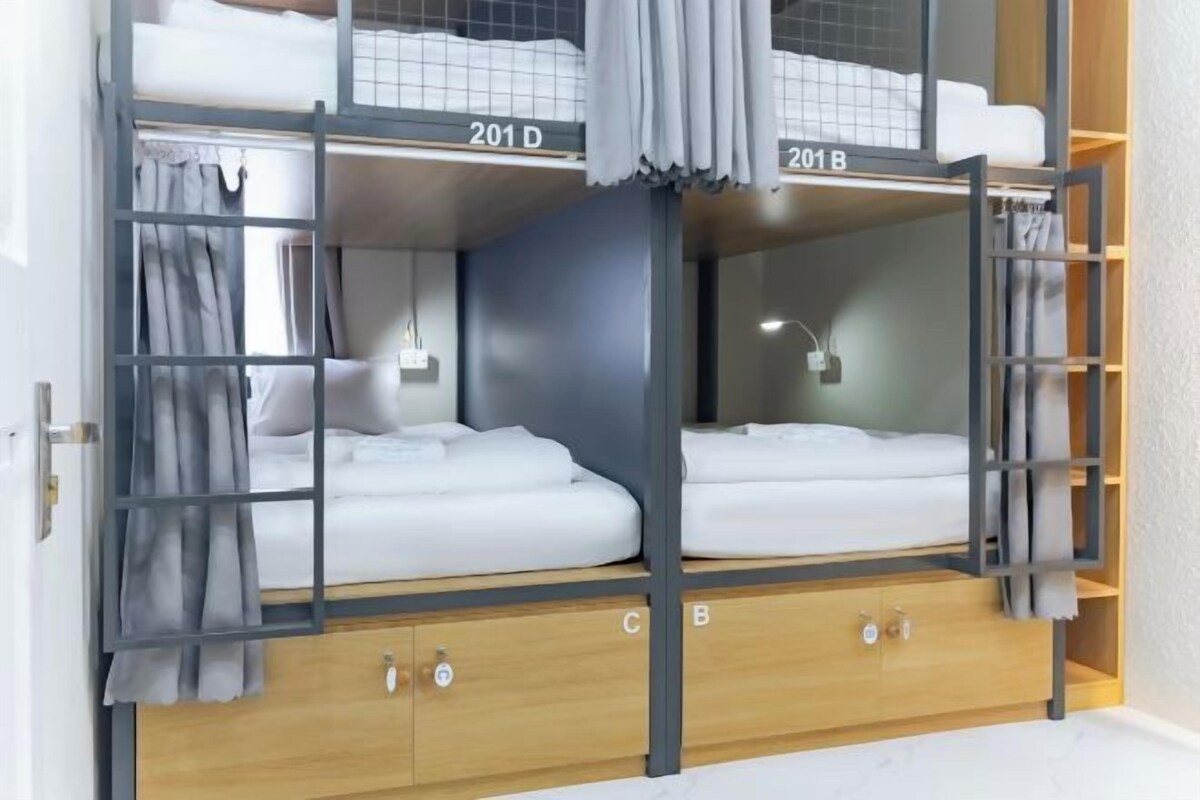 A bunk bed room with two beds labeled 201 D and 201 B, wooden cabinets, and a curtain.
