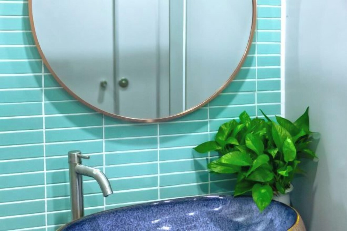 Un baño con un espejo redondo, un lavabo azul y una planta verde.