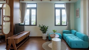 Una sala de estar moderna con un mueble de televisión de madera, un sofá verde azulado, una mesa redonda de centro y una planta grande en maceta.