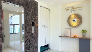 Una moderna área de recepción con una pared de mármol, un letrero de bienvenida enmarcado, un espejo decorativo y una planta pequeña en un estante.