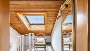 Ein Zimmer mit Holzbalken, einem Oberlicht, einem Sessel, einem Spiegel und einem gemusterten Teppich.