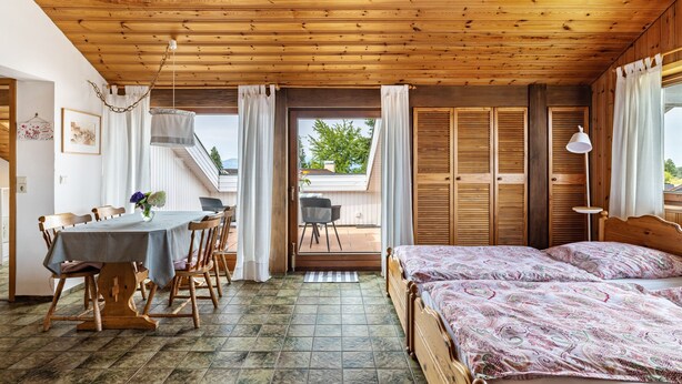 Ein Zimmer mit Holzbalkendecke, einem Bett, einem Tisch mit Stühlen und Blick durch eine Tür.