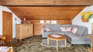 Ein gemütliches Schlafzimmer im Loft-Stil mit schrägem Dach, Holzbalken, einem grauen Sofa, einem Holzkabinett und einem kleinen runden Tisch.