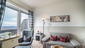 A modern living room with a grey sofa, a grey armchair, a wooden side table, a radiator, a floor lamp, and a window with a view. - Apartment 'Harzperle Nr 6' with Mountain View, Balcony and Wi-Fi (Braunlage)