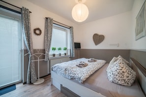 Une chambre à coucher avec un lit, une fenêtre avec des rideaux, un luminaire fixé au mur, une décoration en forme de cœur et un radiateur.