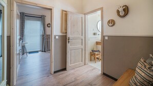 A hallway with wooden flooring, a door leading to a room, a small table with a chair, and wall decorations including a wreath and a circular piece with an anchor design. - Apartment 'Harzperle Nr 6' with Mountain View, Balcony and Wi-Fi (Braunlage)
