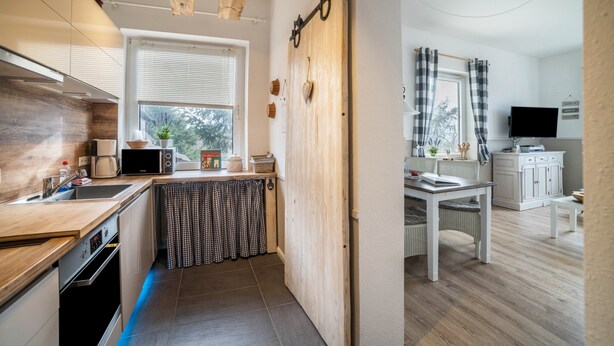 A modern kitchen with a wooden ceiling, a dining area with a white table, and a TV in a corner. - Apartment 'Harzperle Nr 6' with Mountain View, Balcony and Wi-Fi (Braunlage)