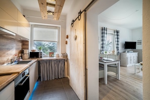 Une cuisine moderne avec un plafond en bois, un coin repas doté d’une table blanche et un téléviseur placé dans un coin.