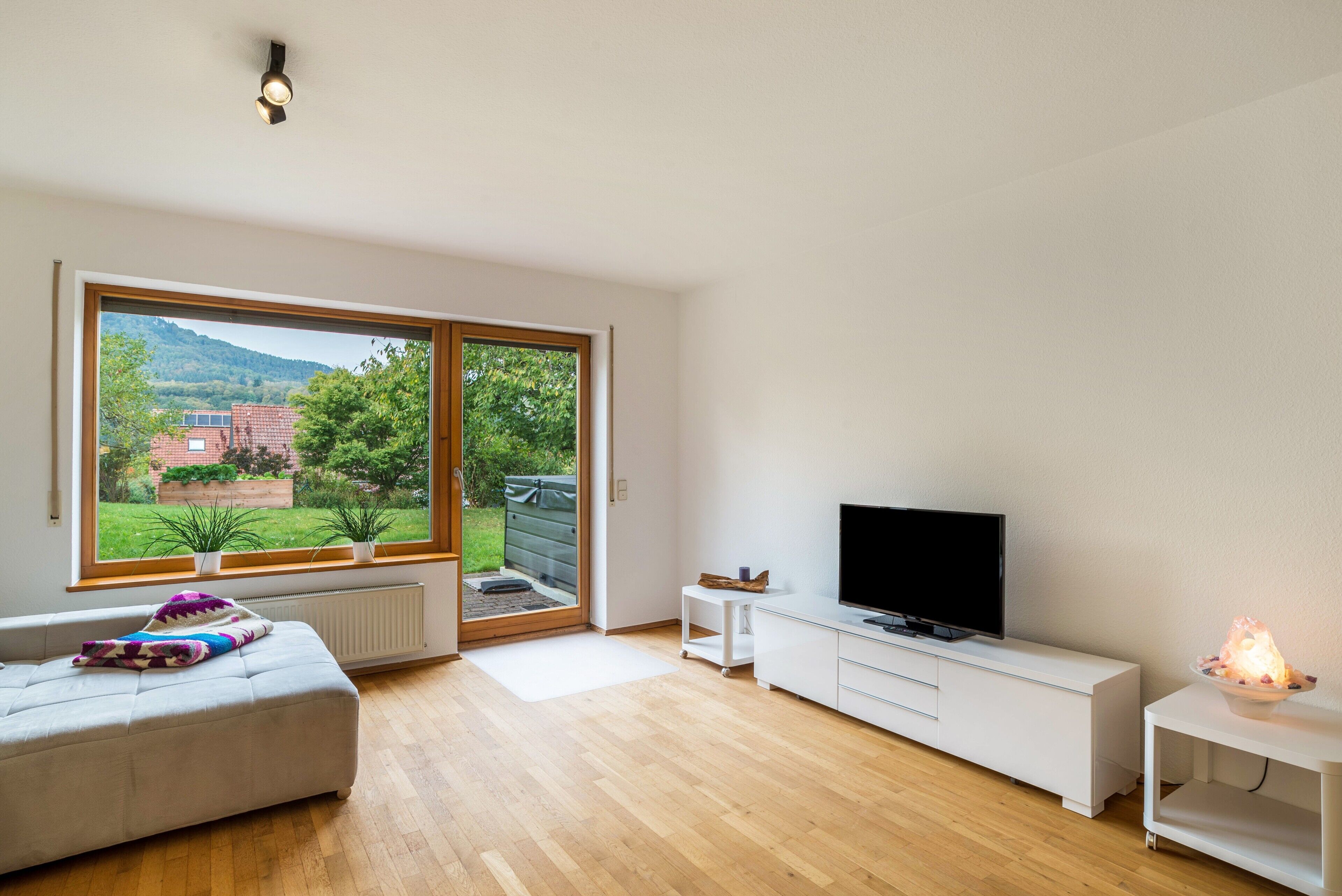 Ein modernes Wohnzimmer mit großem Fenster, einer Couch, einem Fernseher und einem Kamin.