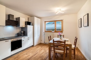 A compact kitchen with modern appliances, a dining area with wooden furniture, and a window with a view of a building. - Apartment 'Gartenblick' with Wi-Fi (Annweiler)