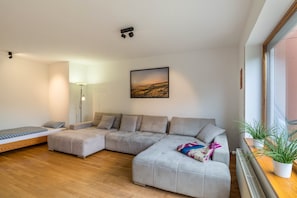A modern living room with a sectional sofa, a small bed, a floor lamp, a framed landscape painting, and a potted plant. - Apartment 'Gartenblick' with Wi-Fi (Annweiler)