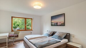 Une chambre à coucher avec un lit, une table de chevet, une chaise, une fenêtre et un tableau accroché au mur.