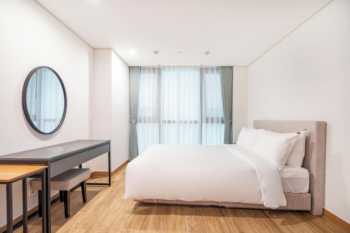 Un dormitorio moderno con cama, escritorio y un ventanal con cortinas.