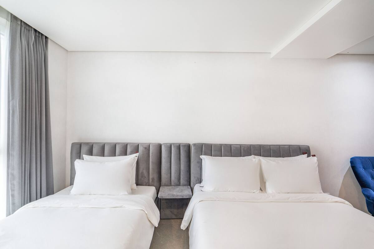 Habitación de hotel con dos camas, cabecera gris y una silla azul.