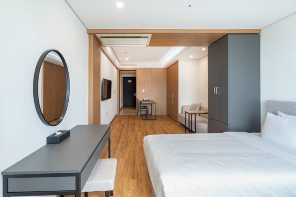 Una habitación de hotel moderna con una cama grande, un escritorio con silla, una mesita y un armario.