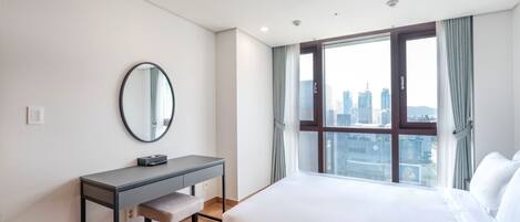 Una habitación de hotel con cama, escritorio, silla, espejo redondo y ventana con vista a la ciudad.