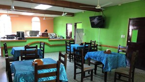 A restaurant with multiple tables covered with blue tablecloths, wooden chairs, and a green wall. - Hotel del Carmen (San Felipe)