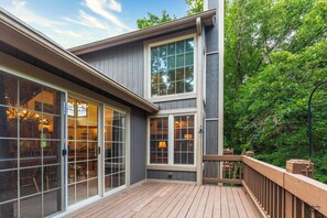 Une maison moderne dotée de grandes portes-fenêtres coulissantes, d ’une terrasse en bois et offrant une vue sur une végétation luxuriante.