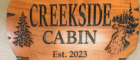 A wooden sign with the text "CREEKSIDE CABIN" and "Est. 2023" indicating the name and establishment year of a cabin.
