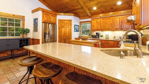Una cocina con armarios de madera, encimera de granito, electrodomésticos de acero inoxidable y taburetes de bar.