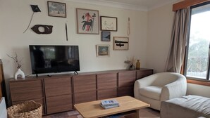 A living room with a TV, wooden cabinet, two sofas, a coffee table, and wall art. - Sun-drenched with spectacular views. Central location for exploring Bruny. (Alonnah)