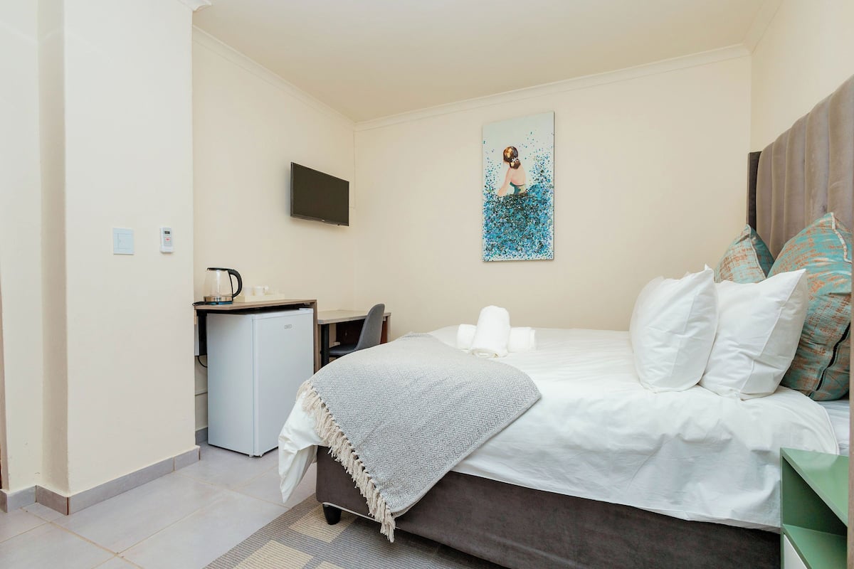 Una habitación de hotel con cama, escritorio, televisión y un cuadro en la pared.